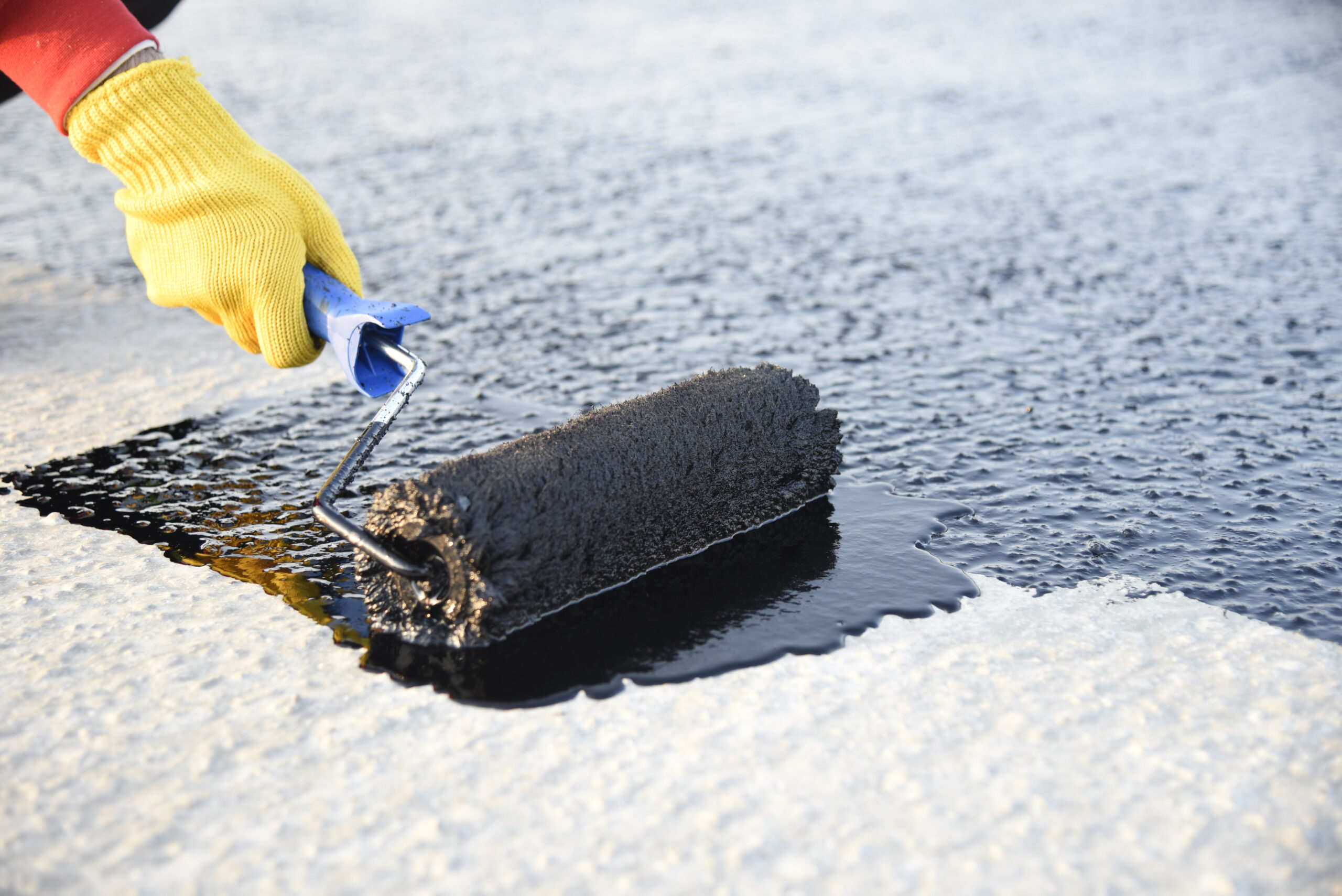 roofer-worker-painting-black-coal-tar-bitumen-concrete-surface-by-roller-brush
